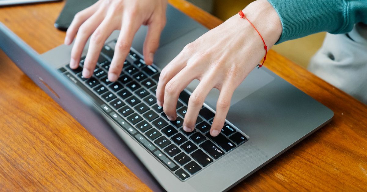 Hände tippen auf einer Laptop-Tastatur auf einem Holztisch
